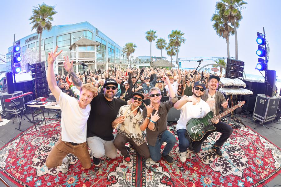 The band on stage with friends in front of the crowd, daytime outdoor show