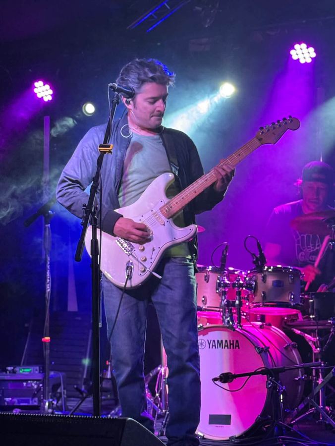 Musician playing a white guitar on a purple-lit stage