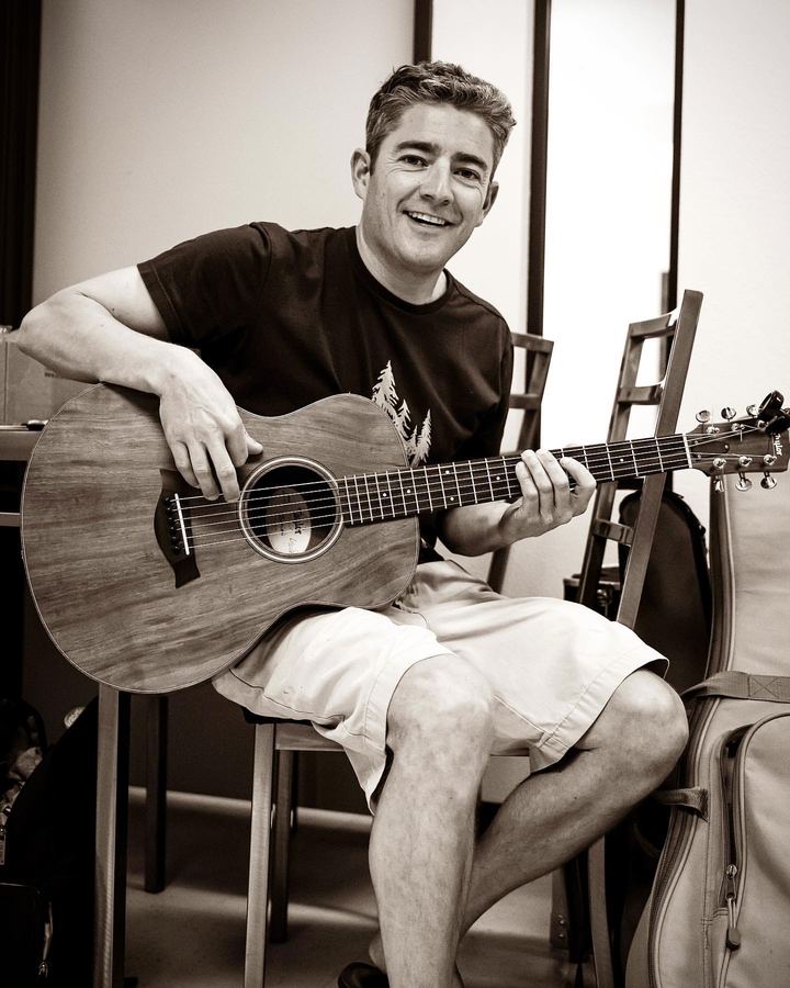 Musician seated with an acoustic guitar, smiling
