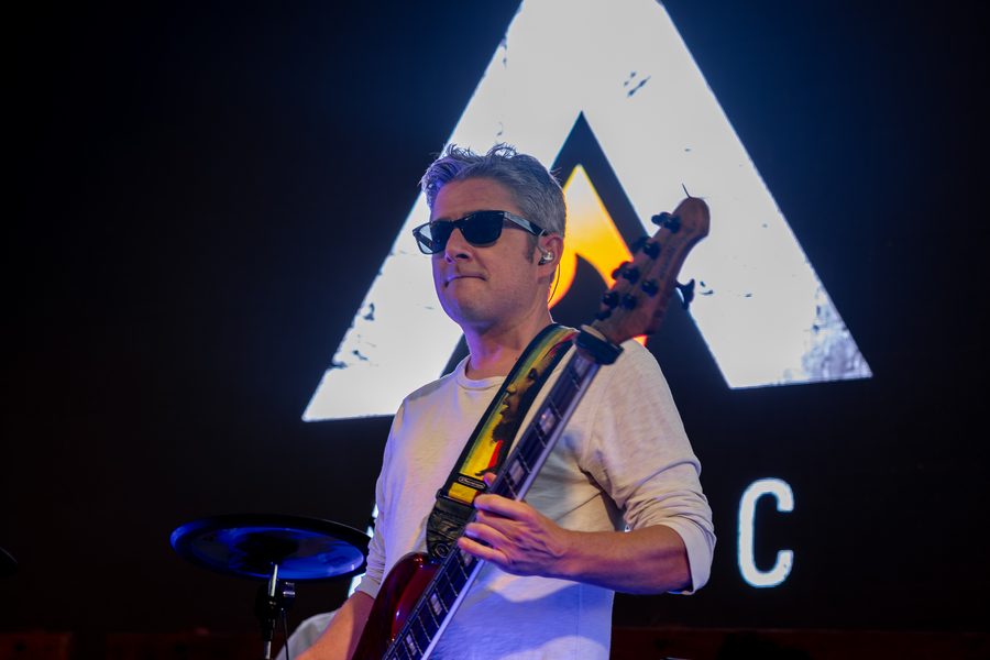 Bassist in front of the glowing Alific backdrop on a dark stage