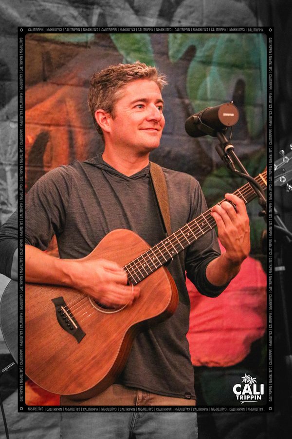 Musician playing an acoustic guitar in front of a painted mural