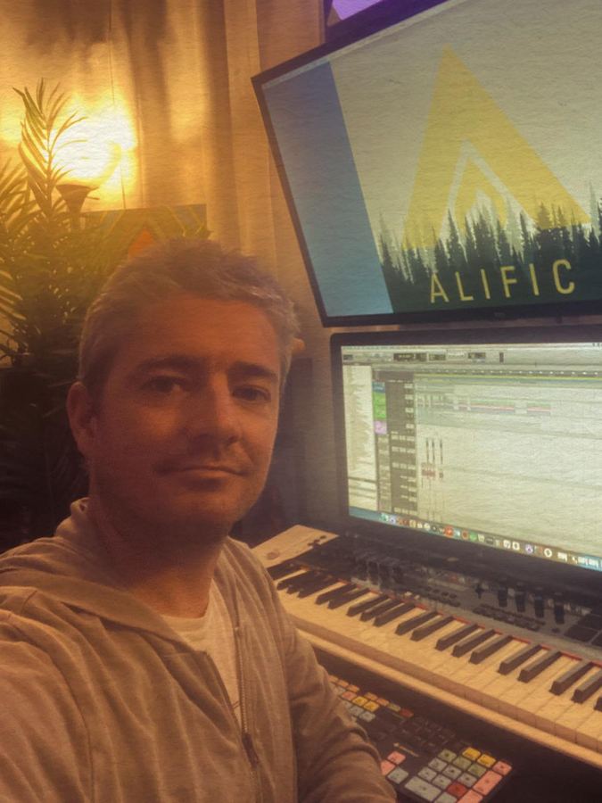 Alific at his studio desk with the Alific logo on the screen behind him